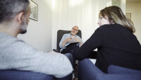 Bildet viser en mannlig terapeut som er vendt mot leseren. Foran ham sitter en mann og ei dame, som vi ser ryggen på.