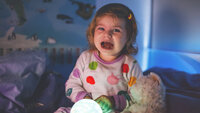 Bildet viser ei lita jente som sitter gråtende i senga. Foran seg holder hun ei lyslampe