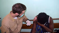Bildet viser en sykepleierstudent på utveksling i Afrika som steller et stort sår på skulderen til en ung dame