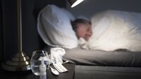 Bilde av person til sengs med forkjølelsesmidler på nattbordet