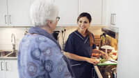 Bildet viser en kvinnelig sykepleier som smiler og snakker med en eldre kvinne