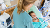Bildet viser en intensivsykepleier som overvåker en pasient i en sykehusseng