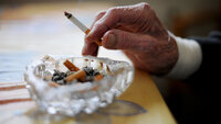 Bildet viser en hånd som holder en sigarett over et askebeger