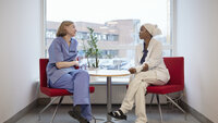 Bildet viser to sykepleiere som sitter og prater sammen ved et vindu