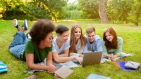 Bildet viser en gjeng studenter som jobber sammen på en laptop utendørs