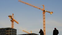 Bildet viser en byggeplass med to mennesker i siluett i forgrunnen