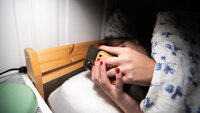 Bildet viser en person som scroller på telefonen i senga.