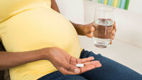 Bildet viser en gravid kvinne som holder frem en tablett og et glass vann