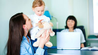 Bildet viser en mor som løfter sitt barn. De sitter foran pulten til helsesøsteren, som skimtes i bakgrunnen.