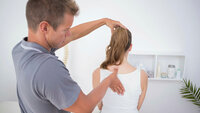 Bildet viser en mannlig terapeut som undersøker ryggen til en kvinnelig pasient.