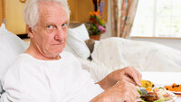 Bildet viser en eldre mann i en sykehusseng som har fått servert et måltid mat på sengen.