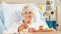 Pasient får mat servert i sykehusseng