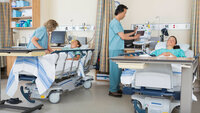Bildet viser to pasienter og to sykepleiere som står ved sengene deres på postoperativen.