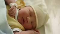 Bildet viser en nyfødt baby påkledd i sengen.