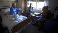Bildet viser en syk, eldre mann i en sykehusseng. Han har besøk av barn og barnebarn.