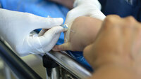 Bilde av en pasient som får lagt inn venekateter i hånden.
