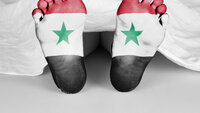 En død kropp under et laken hvor beina stikker frem. Det er tegnet det Syriske flagget på fotsålene.