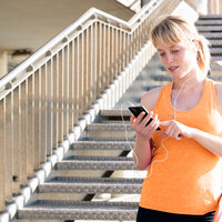 Bildet viser en ung kvinne med høretelefoner som ser på en telefon