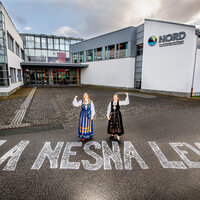 Bildet viser to bunadskledte mennesker utenfor høgskolen i Nesna, på bakken er det skrevet &quot;La Nesna leve&quot;.
