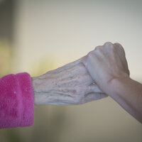 Bildet viser en sykepleier som holder et eldre menneske i hånden