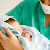 Bildet viser en jordmor som holder et nyfødt barn.