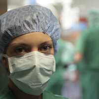 Bildet viser en sykepleier med munnbind foran en operasjonssal