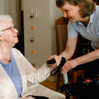 Bildet viser en kvinnelig helsearbeider som har øyekontakt med en eldre kvinnelig pasient som sitter ned.