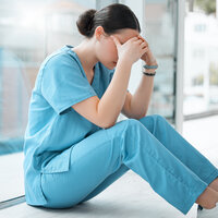 Bildet viser en sykepleier som sitter og er lei seg eller veldig sliten