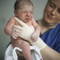 Bildet viser en jordmor som holder opp en nyfødt baby