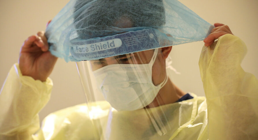 Bildet viser en mann som tar på seg beskyttelsesutstyr, som maske, visir, smittefrakk osv.