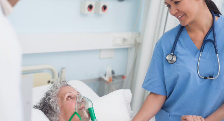 Bildet viser en pasient i sengen med maske, mens en sykepleier står ved siden av